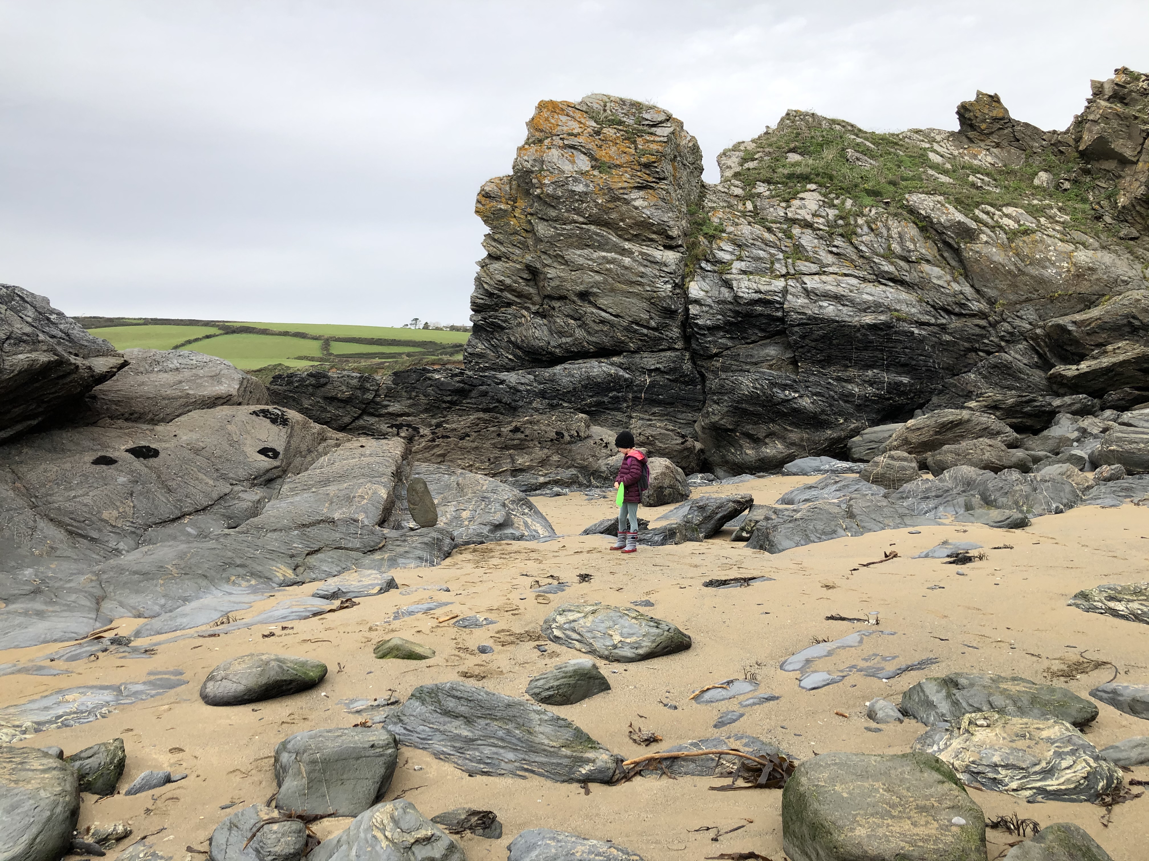 Cornwall with kids: Hemmick Beach - Bella holding green fishing net in front of large grey rocks
