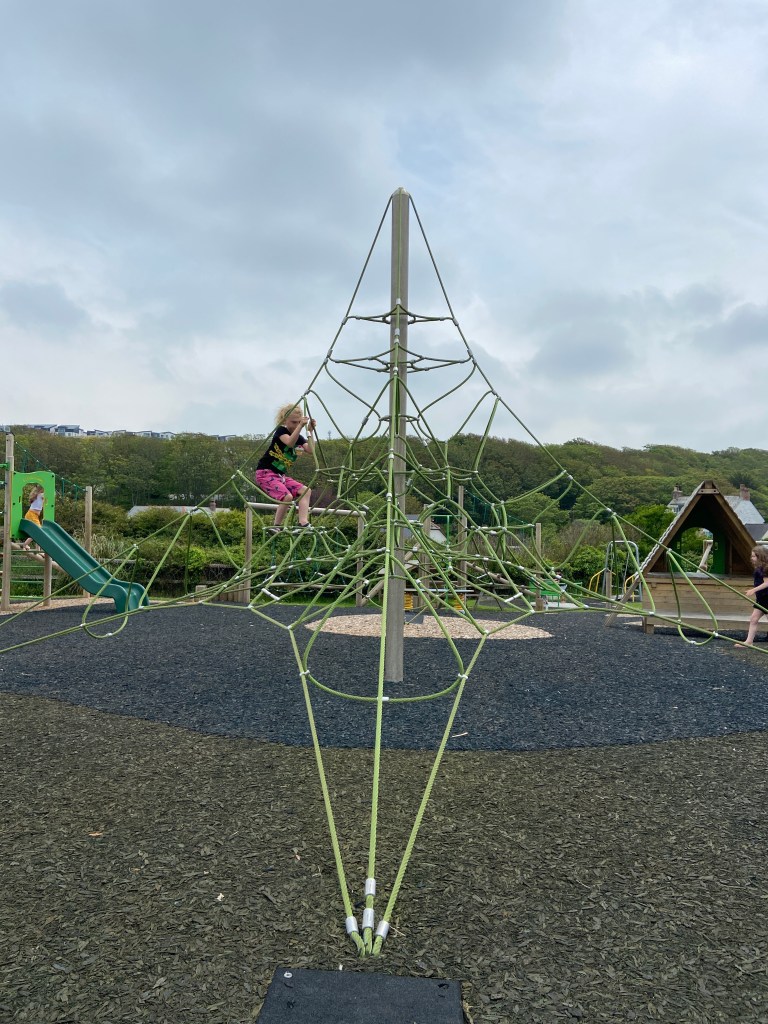 Girl climbing a climbing frame at a play park in Perranporth in Cornwall