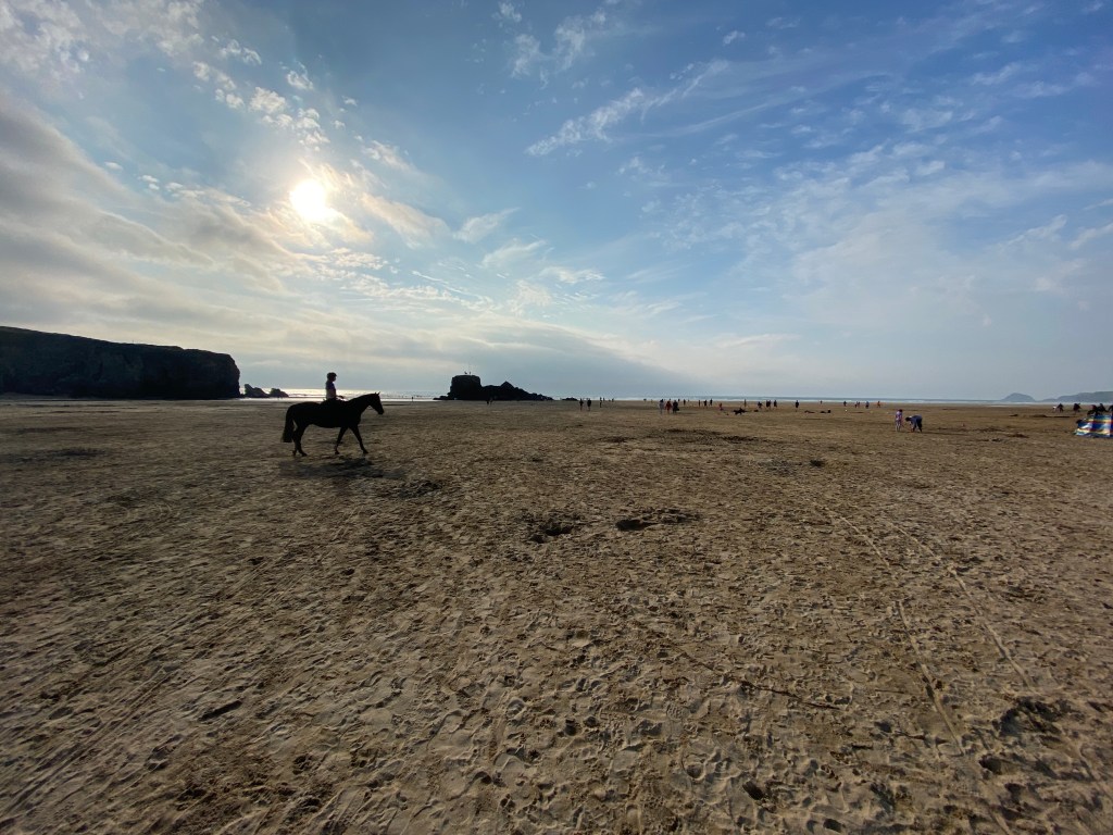 Horse rider riding horse on the beach with the sun setting at Perranporth beach in Cornwall