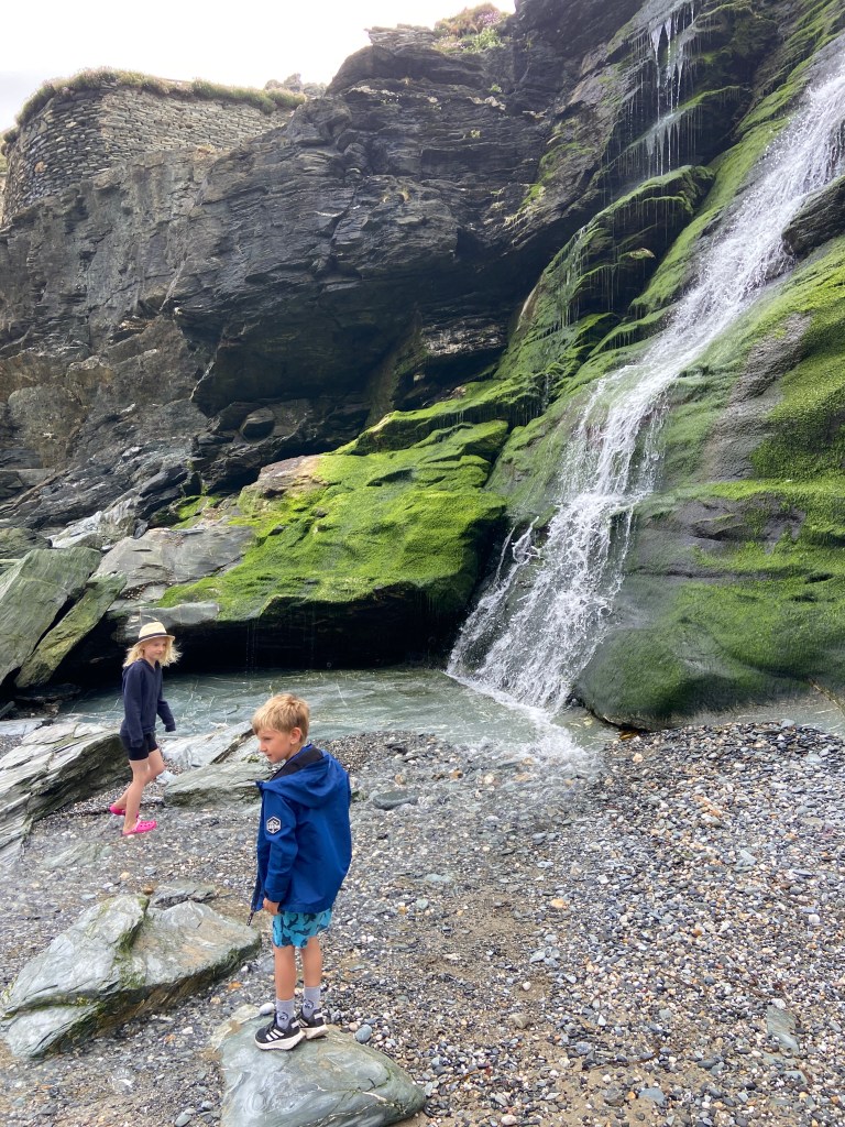 waterfall running down cliffs to beach at Tintagel beach in Cornwall