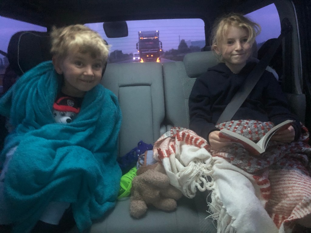Kids in Bongo campervan off on holiday on the motorway, wrapped in blankets as it's 5am