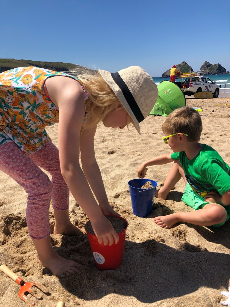kids having fun filling buckets with sand at Holywell beach near newquay cornwall