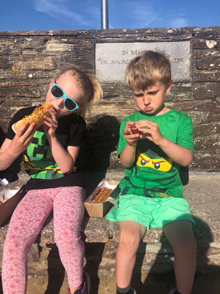 Kids sat on a bench eating vegan hotdogs in Perranporth