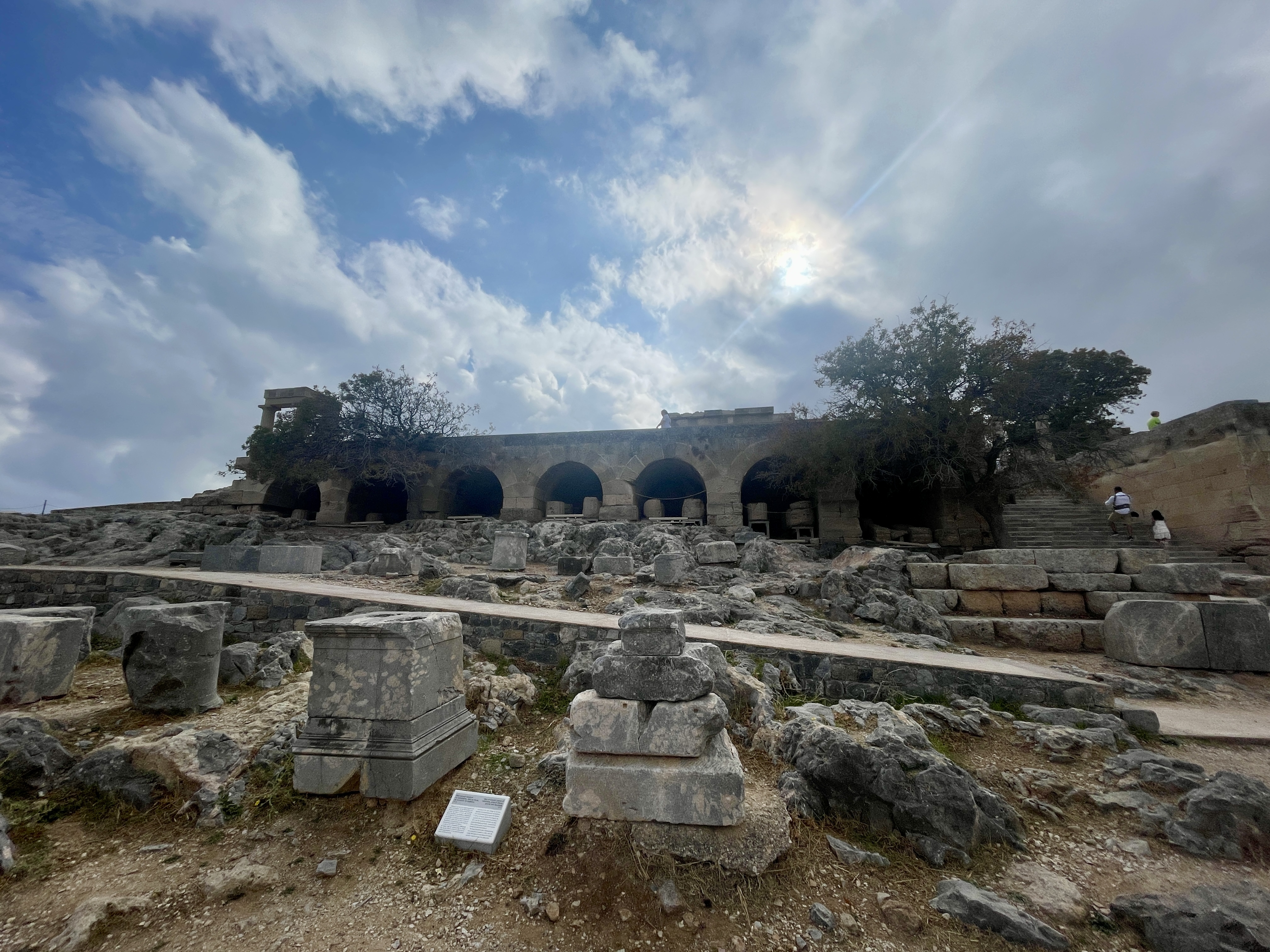 Ancient stone ruins and salvaged architectural pieces scattered across the Lindos Acropolis site