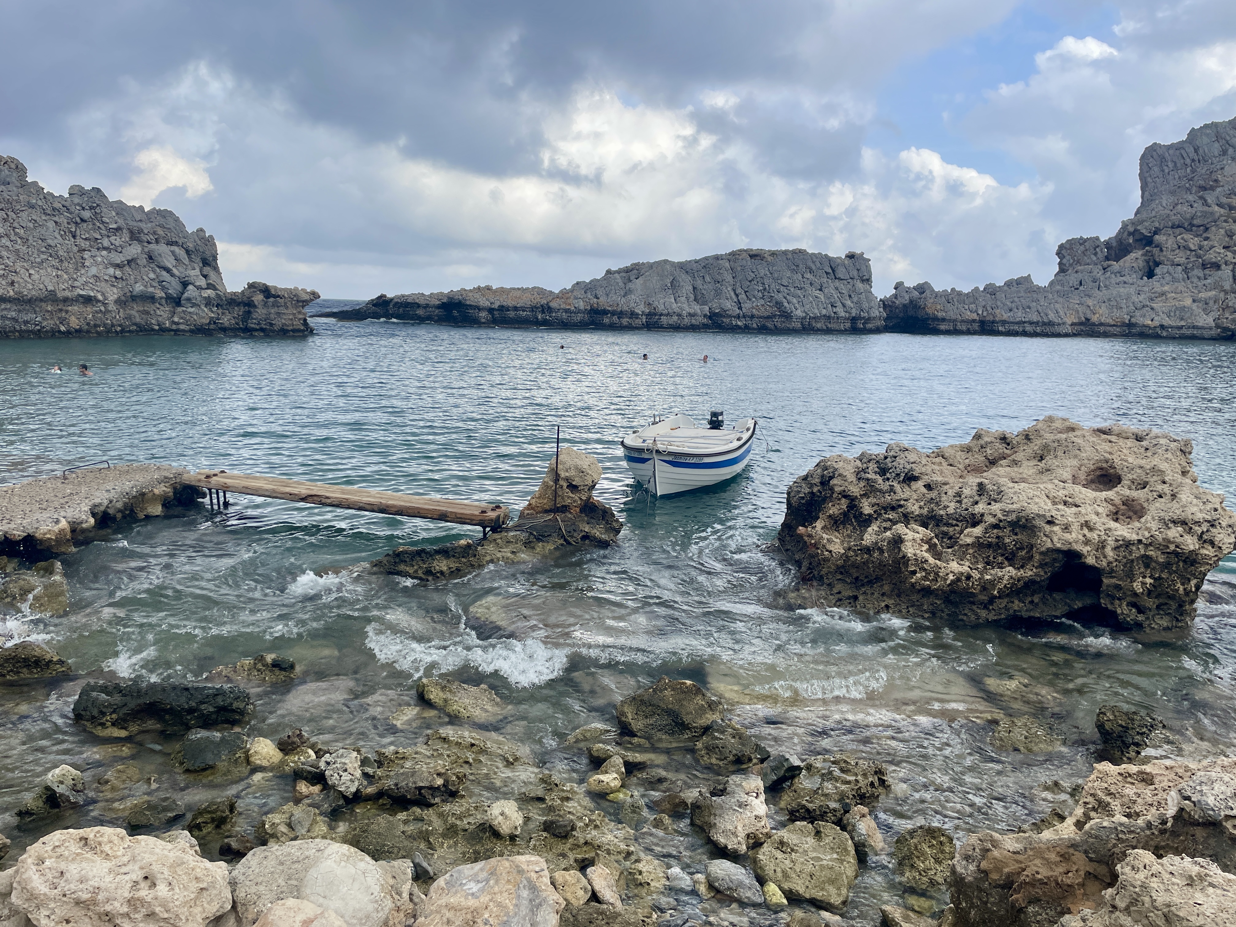 A small boat bobbing in the water next to Mikros Gialos Beach at St Paul's Bay in Lindos, Rhodes
