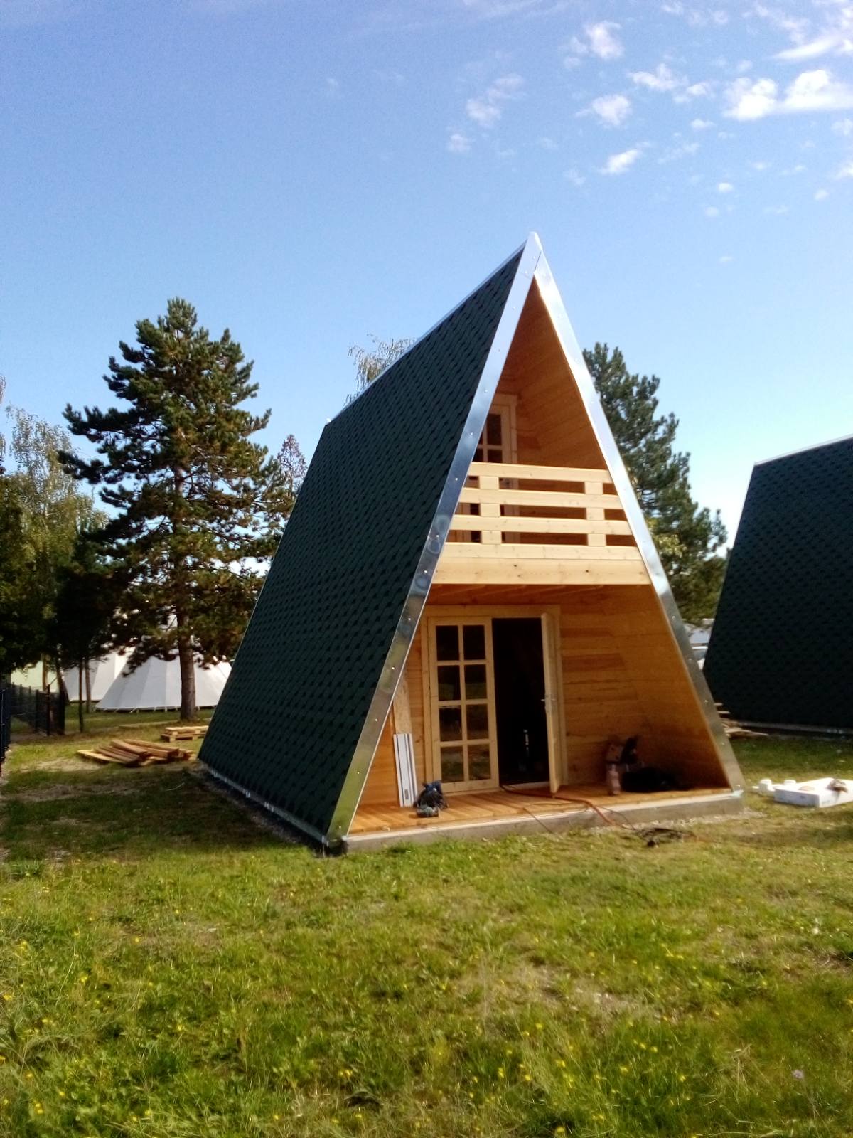 A-frame garden cabin with dark green roof and wooden interior surrounded by trees