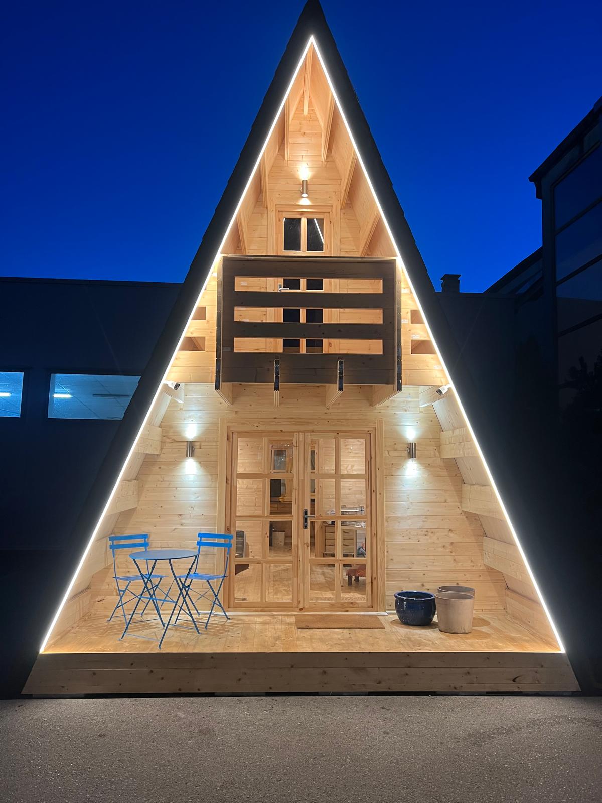 A-frame log cabin illuminated at night with LED lighting and bistro table outside