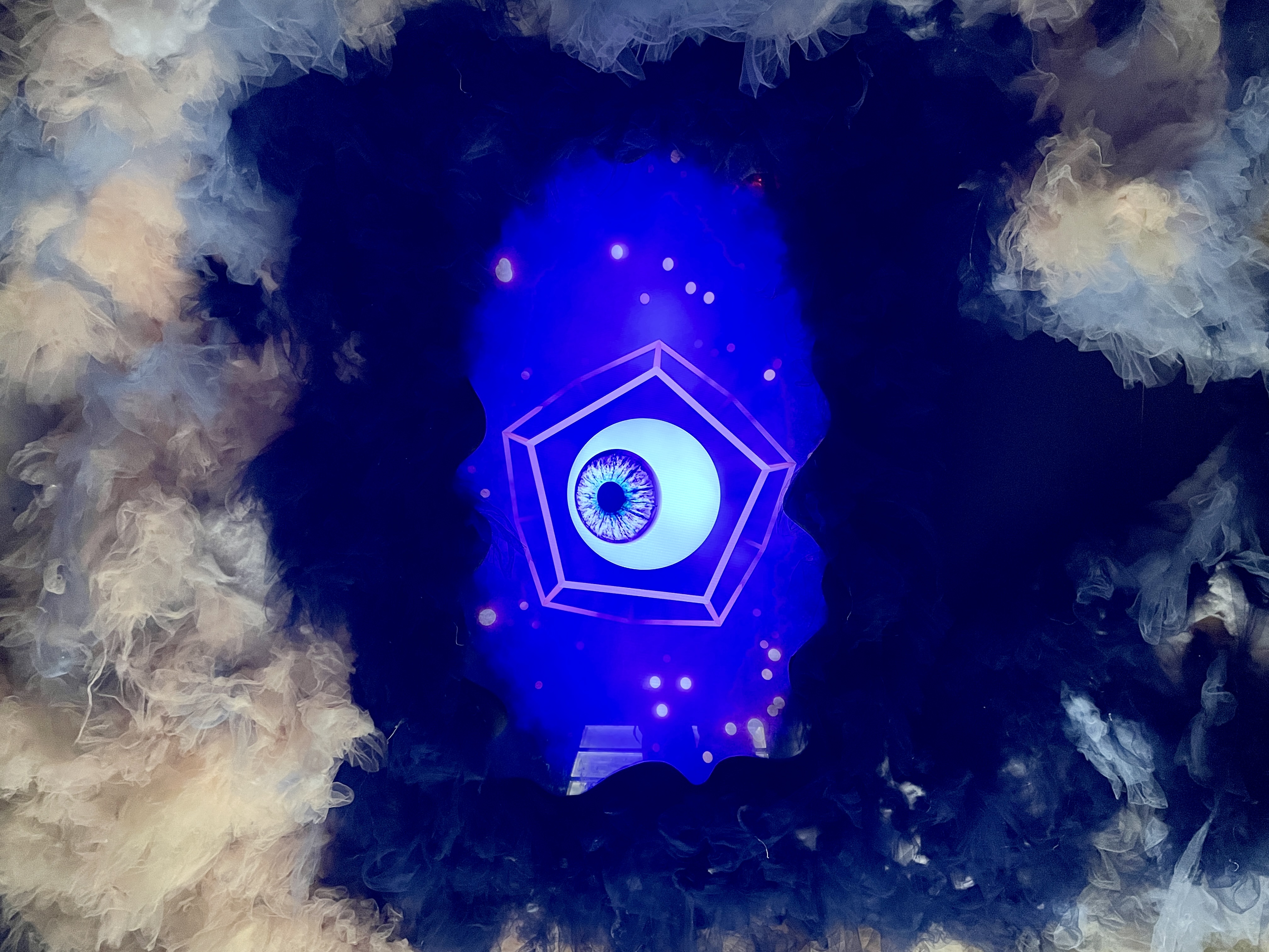 Giant eye in pentagon frame looking down through fluffy clouds at Wake the Tiger Bristol