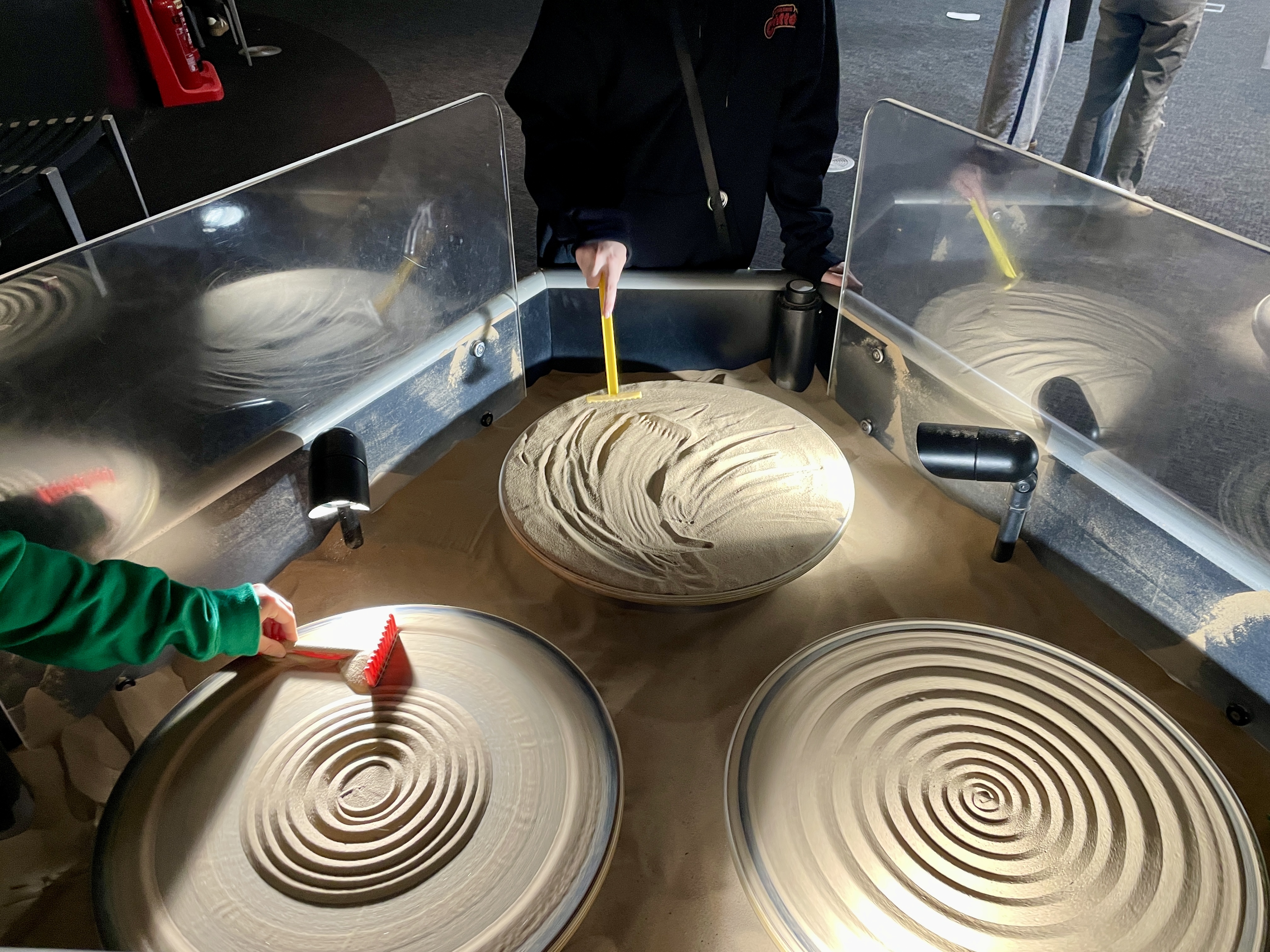 Spinning sand plates with rakes making spiral patterns at We The Curious Bristol